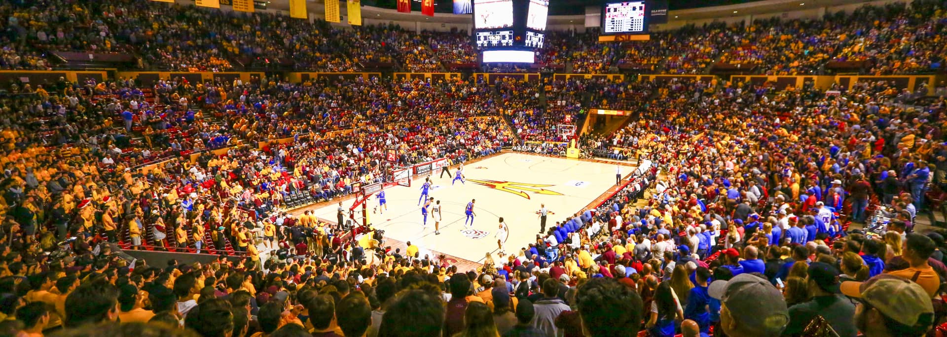 A zoomed out photo of the ASU basketball stadium with the pitchfork logo printed on the court and the stadium full of fans.