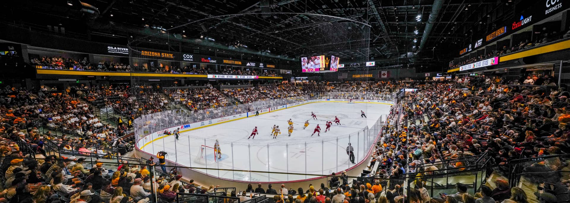 A zoomed out shot of the ASU hockey field with players on the field and the stadium filled with crowds.