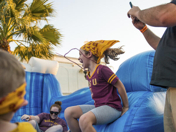 A young girl in an ASU shirt jumps in an inflatable bouncy house.