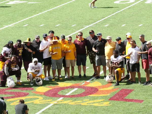 Group photo of ASU players and families on a football field with SOL Devils painted on the grass in front of them.